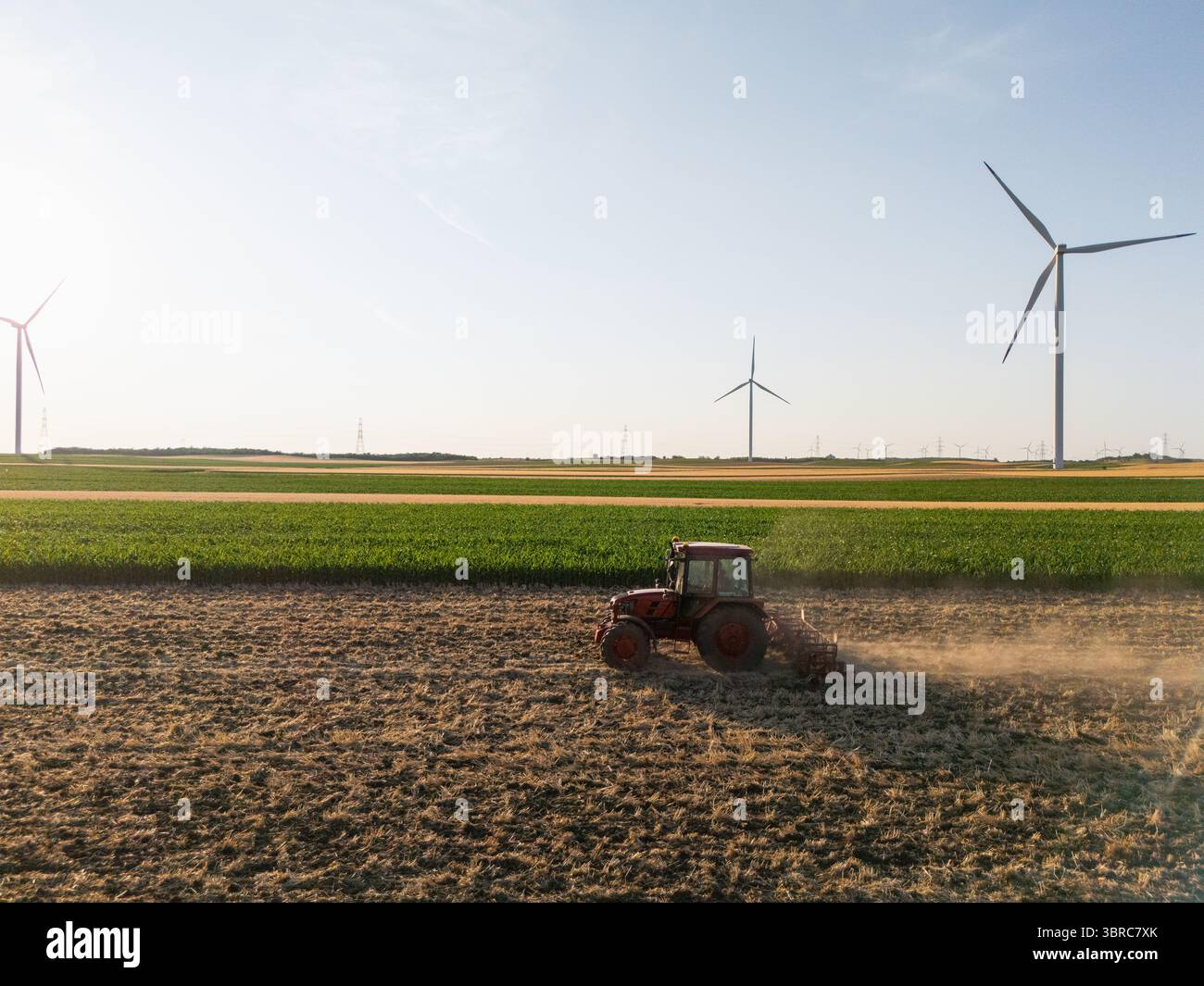 Der landwirtschaftliche Traktor arbeitet auf dem Feld mit Windturbinen. Luftaufnahme. Stockfoto