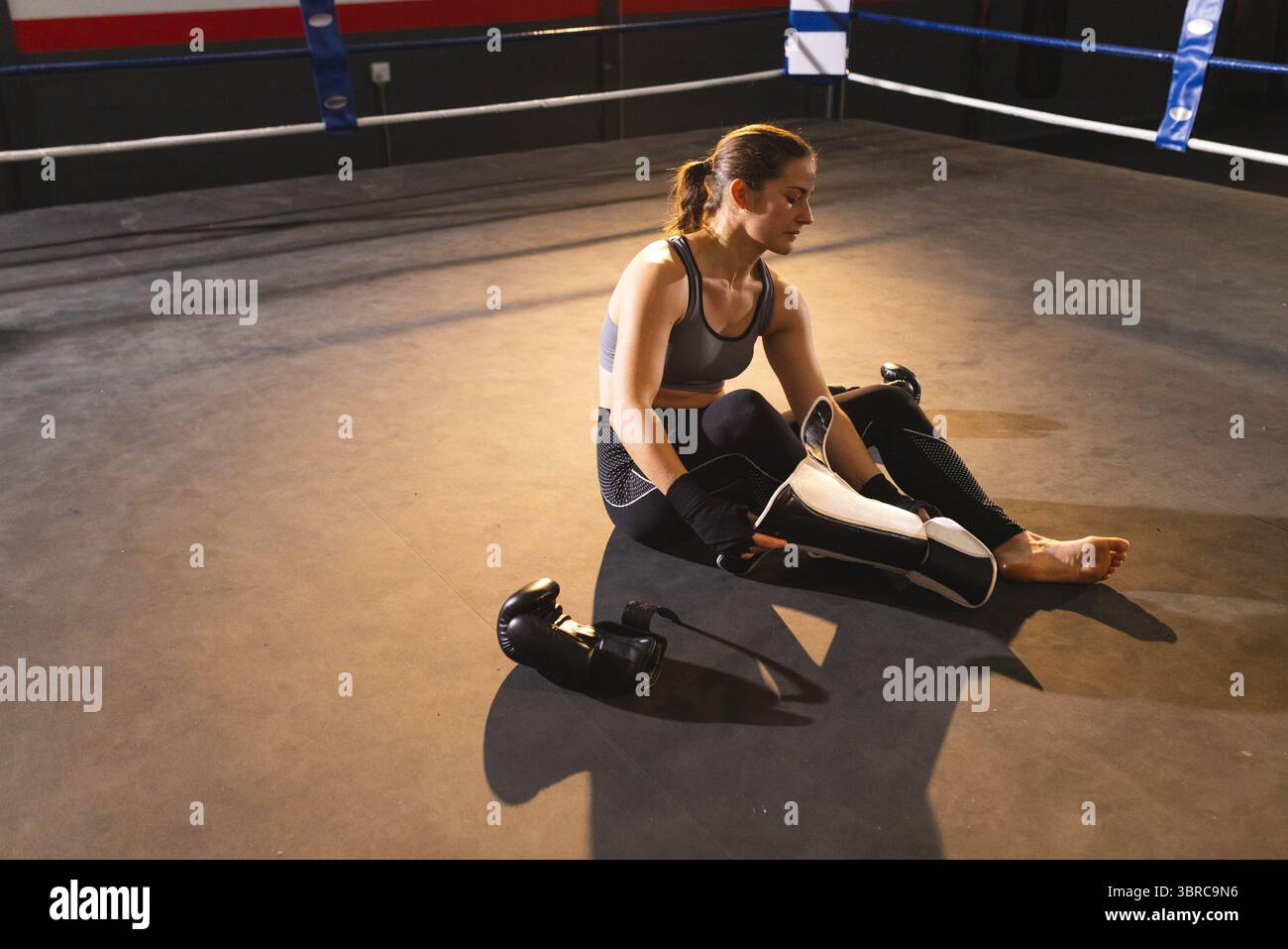 Weibliche Athletinnen tragen Schienbeinschutz auf Boxring-Leinwand, mit Handschuhen in der Nähe blauer Seile Stockfoto