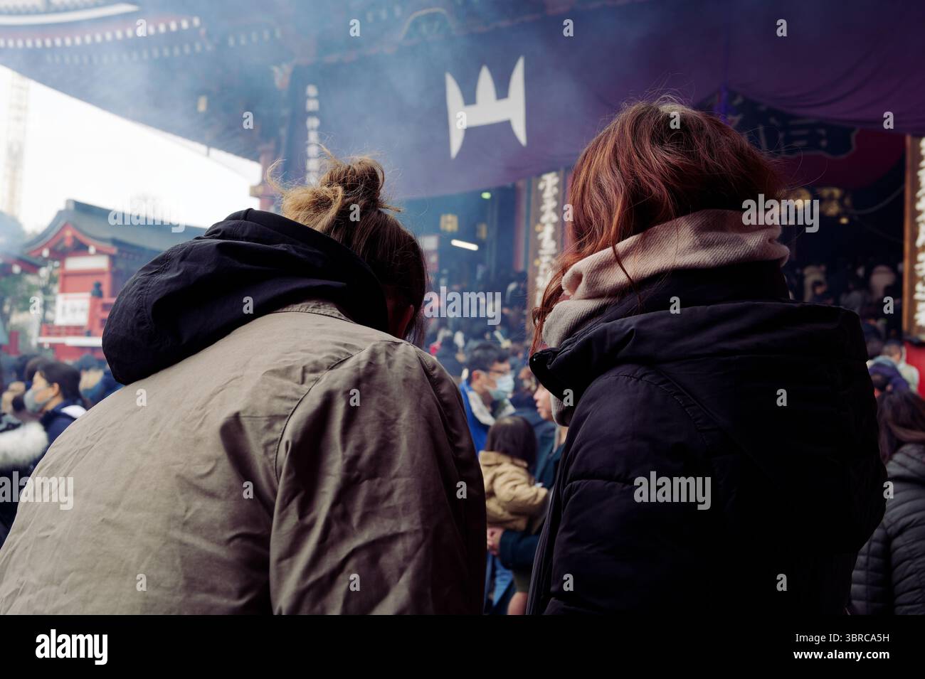 Zwei weibliche Besucher halten im Weihrauchschleier vor dem Eingang des Senso Ji Tempels inne Stockfoto