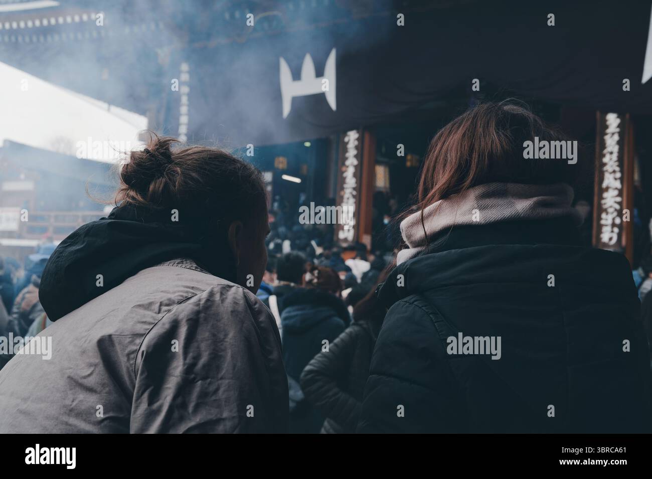 Zwei Besucher halten im Weihrauchschleier vor dem Eingang des Senso Ji Tempels inne Stockfoto