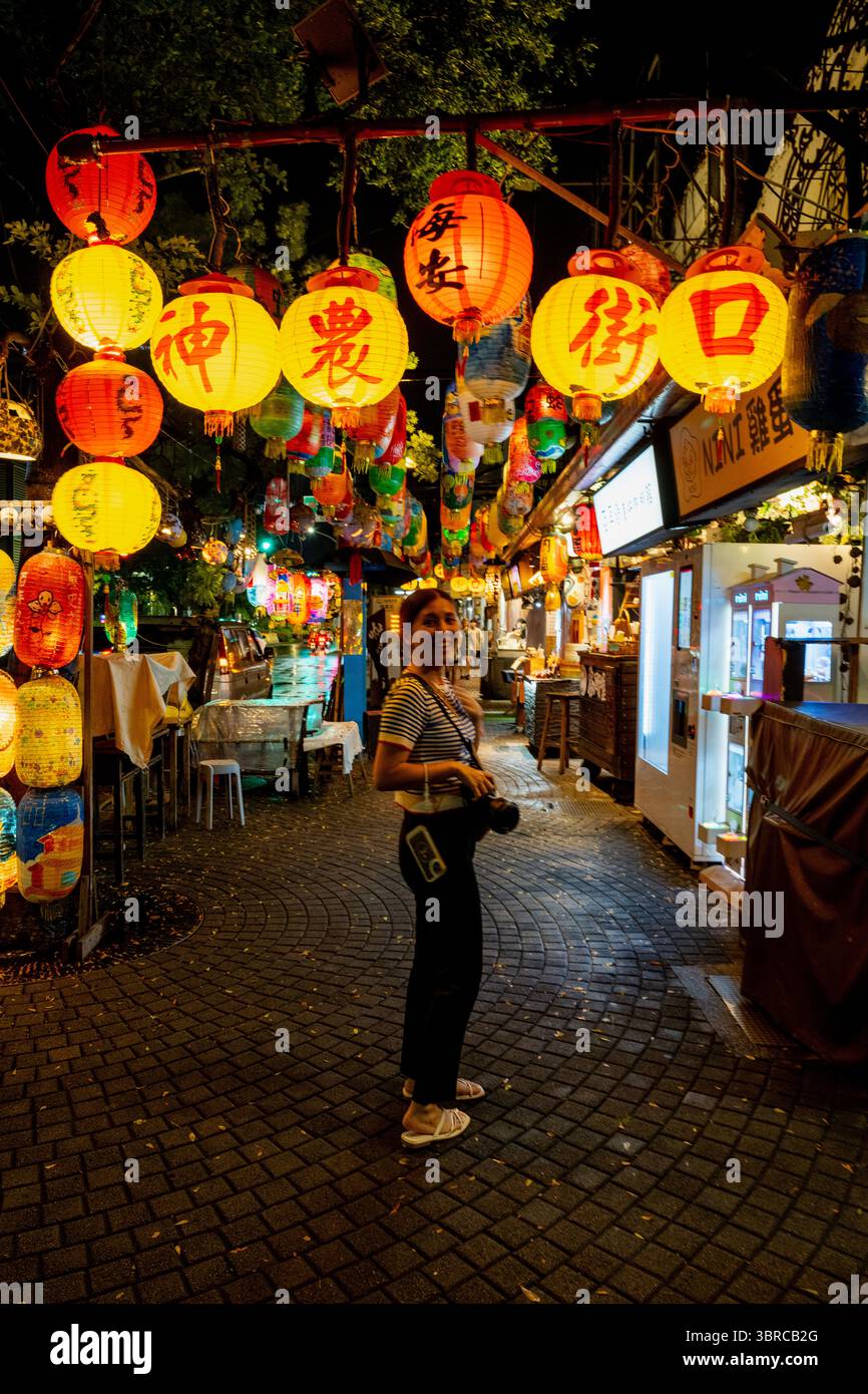 Tainan, Taiwan – 29. Juni 2025: Eine weibliche Touristenin mit Kamera genießt die Laterne-Nacht am Eingang der Shennong Street. Die Straße ist mit dekoriert Stockfoto