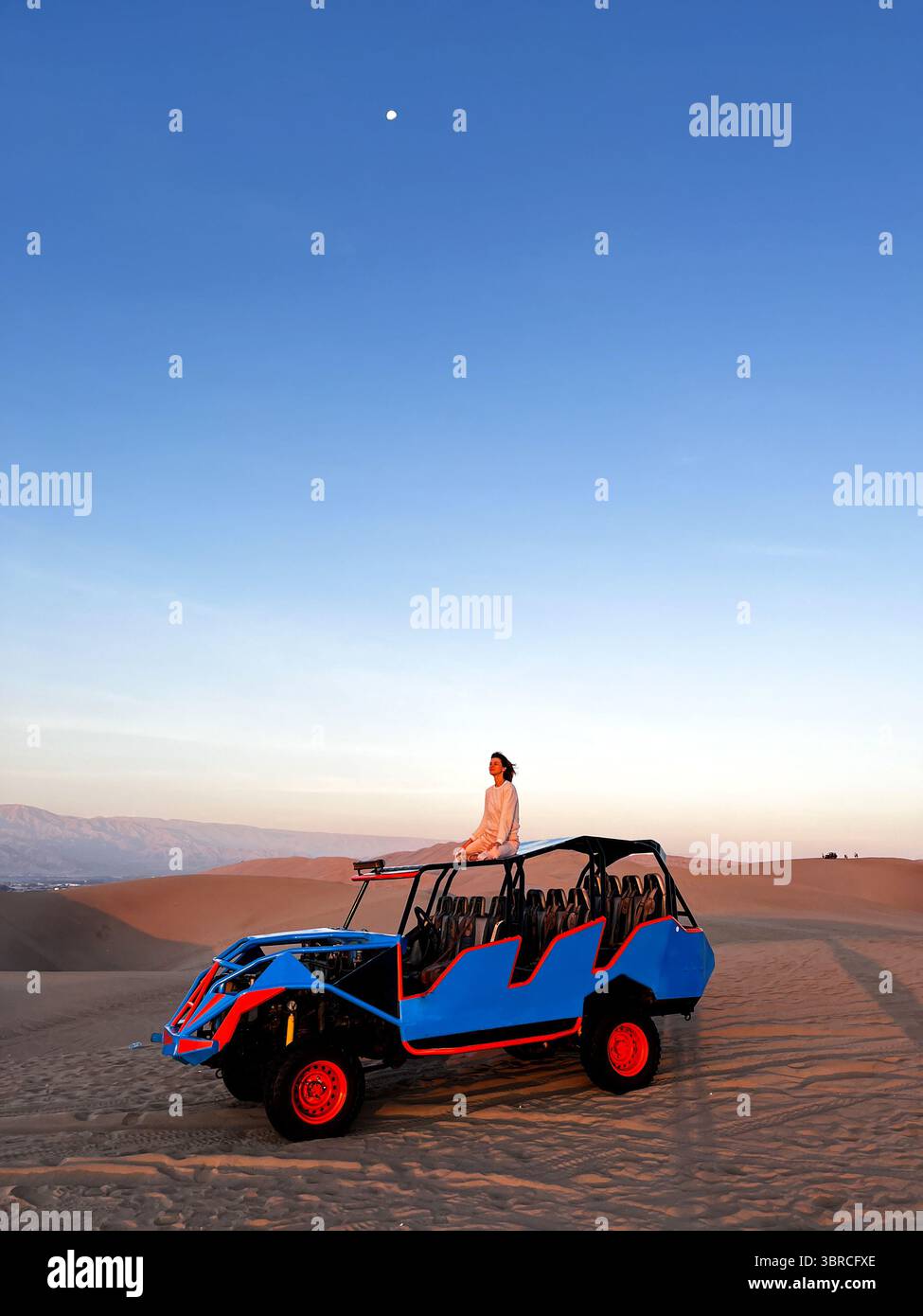 Frau, die auf dem Dach eines Buggys sitzt, der Touristen in der Wüstenregion herumfährt und die wunderschöne, trockene Landschaft von Huacachina, Ica, Peru beobachtet Stockfoto