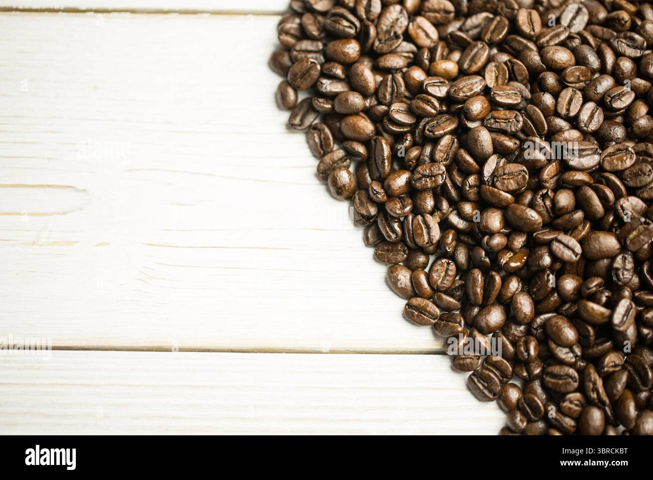 Ein Hügel gerösteter Kaffeebohnen wird in flacher Ausführung auf weiß lackierter Holzdiele gezeigt Stockfoto