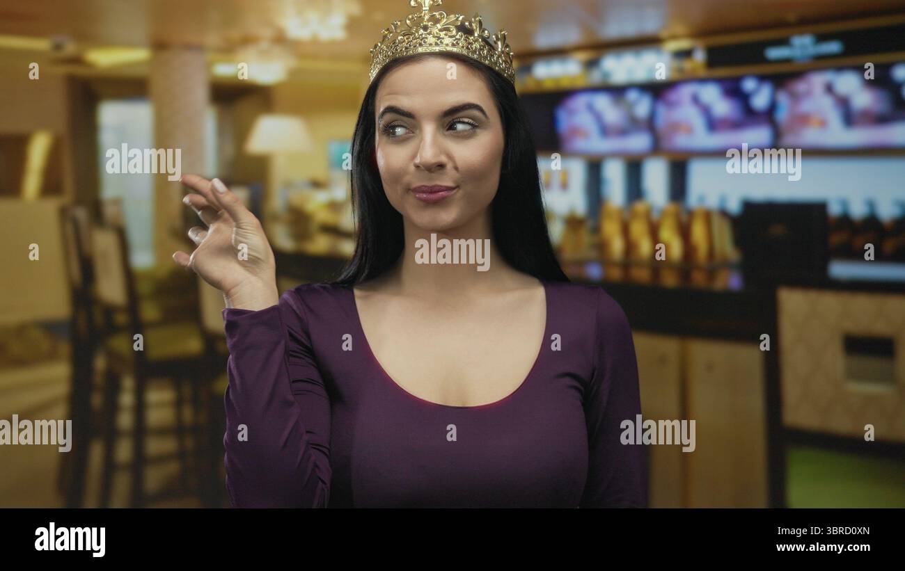 Die hispanische Frau mit Krone drückt den Mund in einem Café mit warmer Beleuchtung und vermittelt Eleganz und Kommunikation in einem Restaurant setti Stockfoto