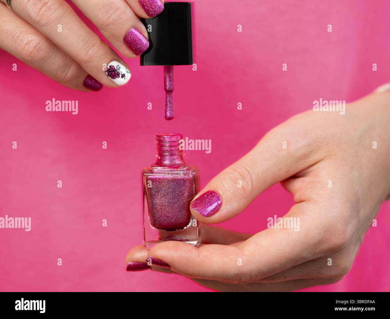 Weibliche Hände mit rosafarbener Maniküre haben eine rosa lila nagellackflasche. Frau mit rosa holographischen nagellackpinsel. Das ästhetische Erscheinungsbild von Rot Stockfoto