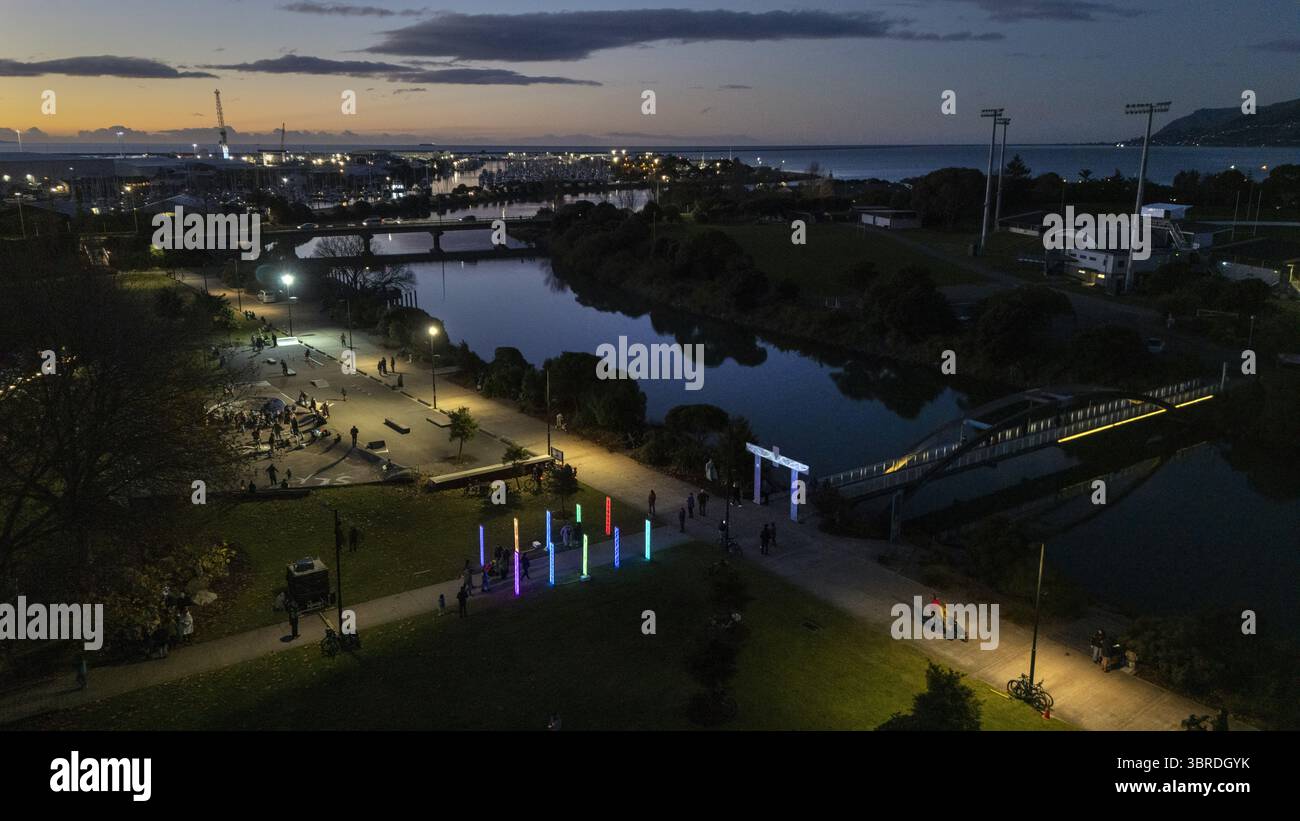 Aus der Vogelperspektive eines ruhigen Flusses, der die Lichter der Stadt reflektiert, mit Menschen, die auf pou rama spazieren, beleuchteten Wegen in der Dämmerung, Nelson, Region Nelson, Neuseeland. Stockfoto