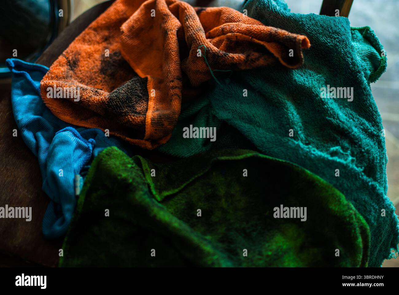 Ein Haufen bunter, schmutziger Lappen, die in der Nähe des Zerkleinerers auf dem Holzstuhl liegen. Alte Garage Stockfoto