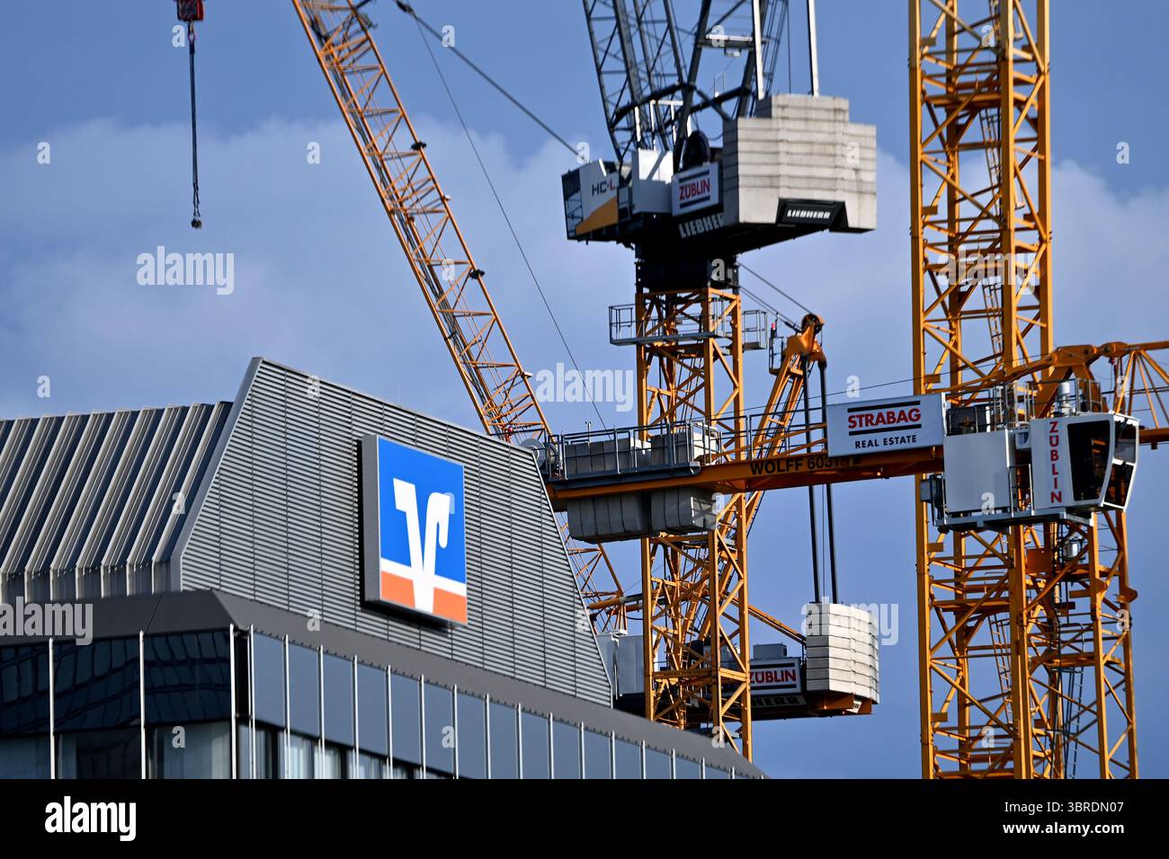München, Deutschland. Juli 2025. Betrefffoto: Volksbank Raiffeisenbank EG, Logo, Banklogo, Firmenlogo, Firmenlogo. Dahinter befinden sich Baukräne, Baustelle? Quelle: dpa/Alamy Live News Stockfoto