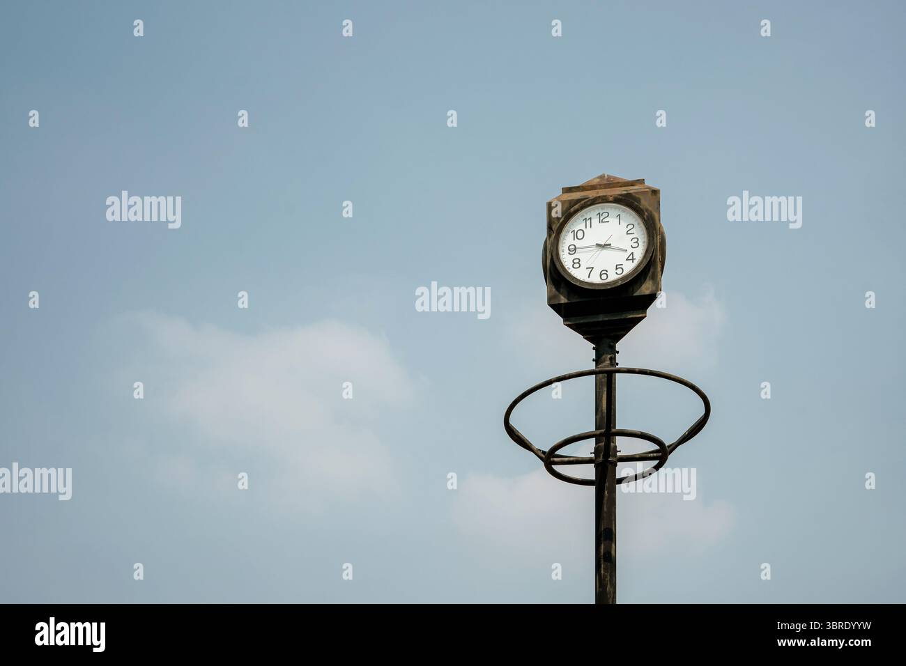 Eine klassische öffentliche Straßenuhr im Vintage-Stil an einem Mast vor einem riesigen blauen Himmel mit weichen weißen Wolken. Ein minimalistisches Konzept des Zeitvertreibens. Stockfoto