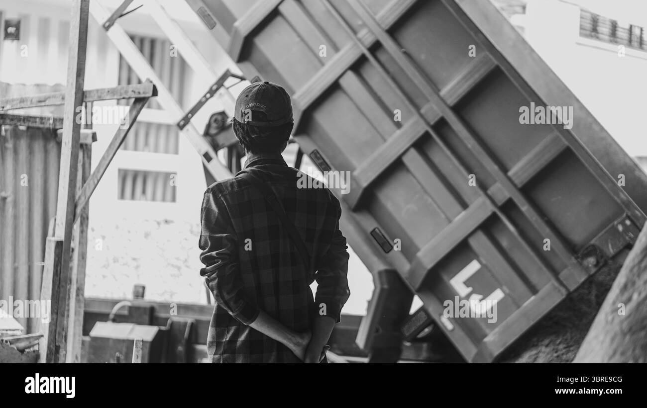 Hinter seiner Stillhaltung bewegt sich sein Verstand. Beobachten, wie der blaue Lkw Sand entlädt – nur der Anfang dessen, was bald zu etwas starkem und dauerhaftem wird Stockfoto