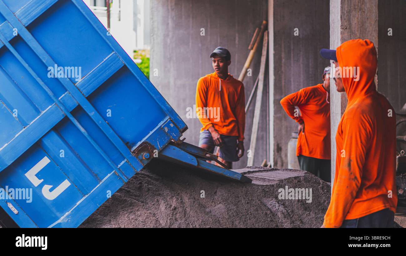 Hinter seiner Stillhaltung bewegt sich sein Verstand. Beobachten, wie der blaue Lkw Sand entlädt – nur der Anfang dessen, was bald zu etwas starkem und dauerhaftem wird Stockfoto