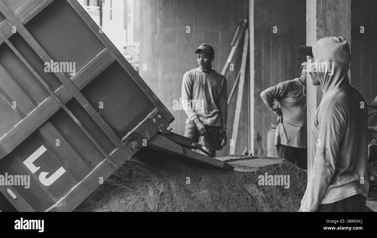 Hinter seiner Stillhaltung bewegt sich sein Verstand. Beobachten, wie der blaue Lkw Sand entlädt – nur der Anfang dessen, was bald zu etwas starkem und dauerhaftem wird Stockfoto