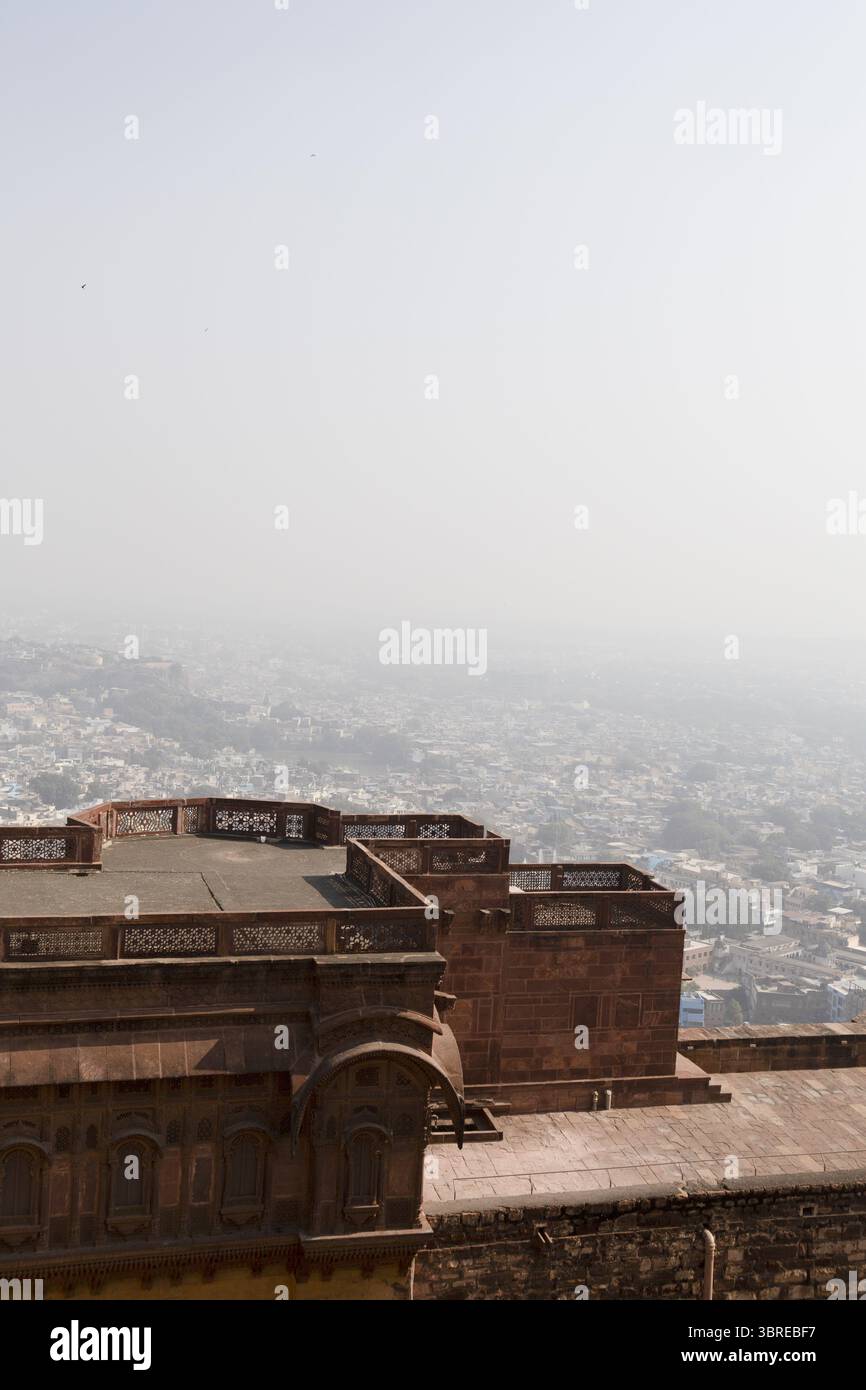 Blick auf die roten Sandsteinmauern des historischen Mehrangarh Forts mit Blick auf die raue Stadtlandschaft darunter, getaucht in das sanfte Licht der Dämmerung, Jodhpur, Rajasthan, Indien. Stockfoto