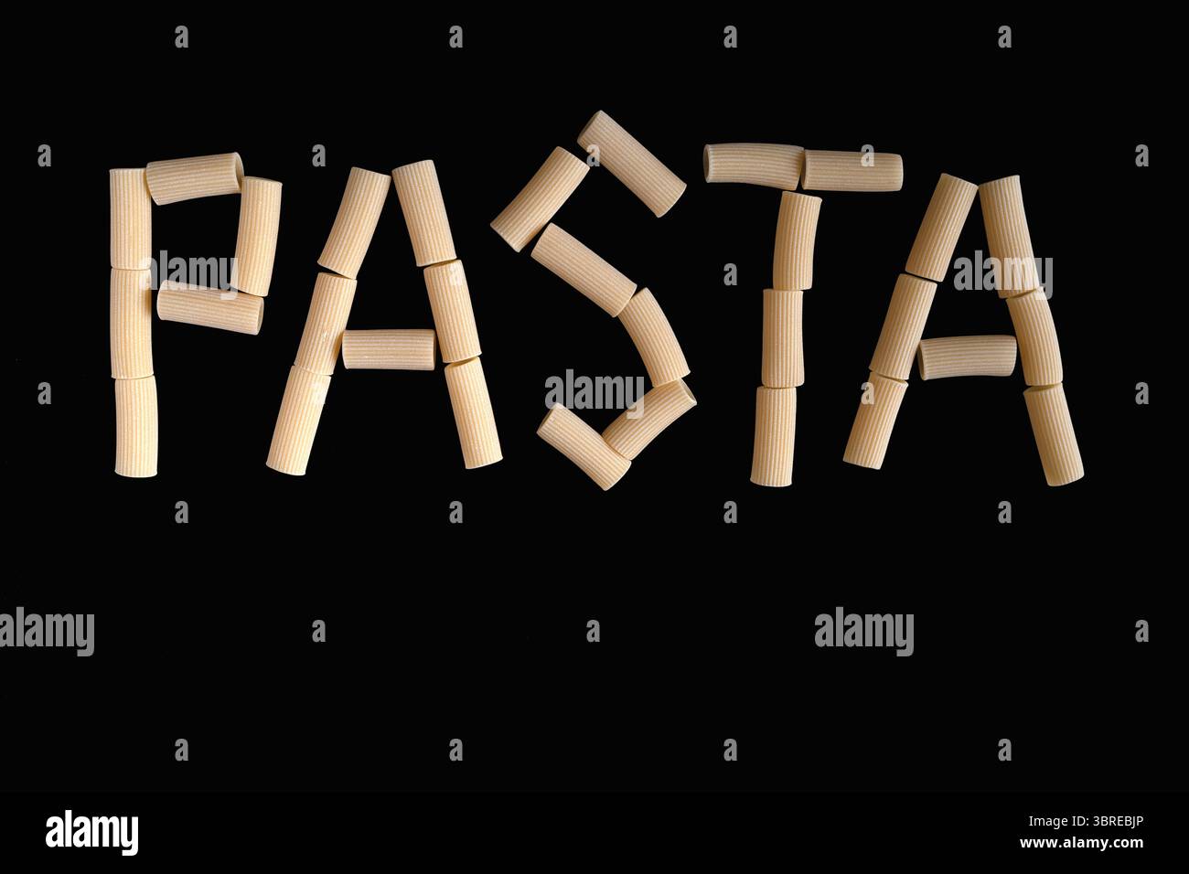 Das Wort „PASTA“ wurde aus natürlichen, nicht gekochten Rigatoni-Nudelröhrchen gebildet, die deutlich auf einem minimalistischen schwarzen Hintergrund abgebildet sind Stockfoto