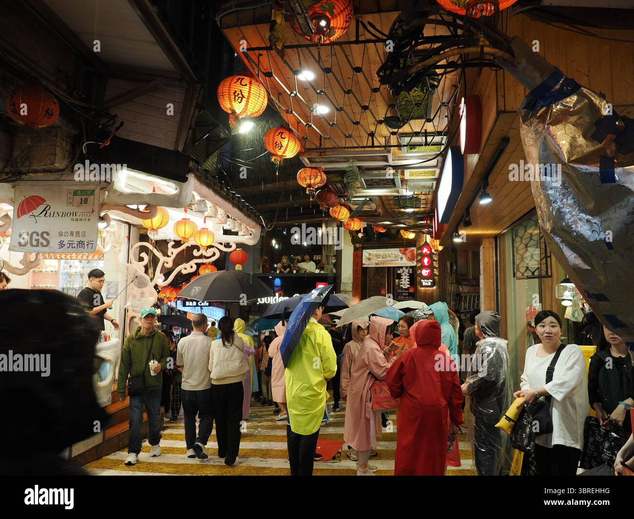 Jiufen, Taiwan - 8. November 2024 - Touristen in Regenkleidung und mit Sonnenschirmen spazieren nachts durch die feuchten Gassen der Jiufen Old Street. Stockfoto