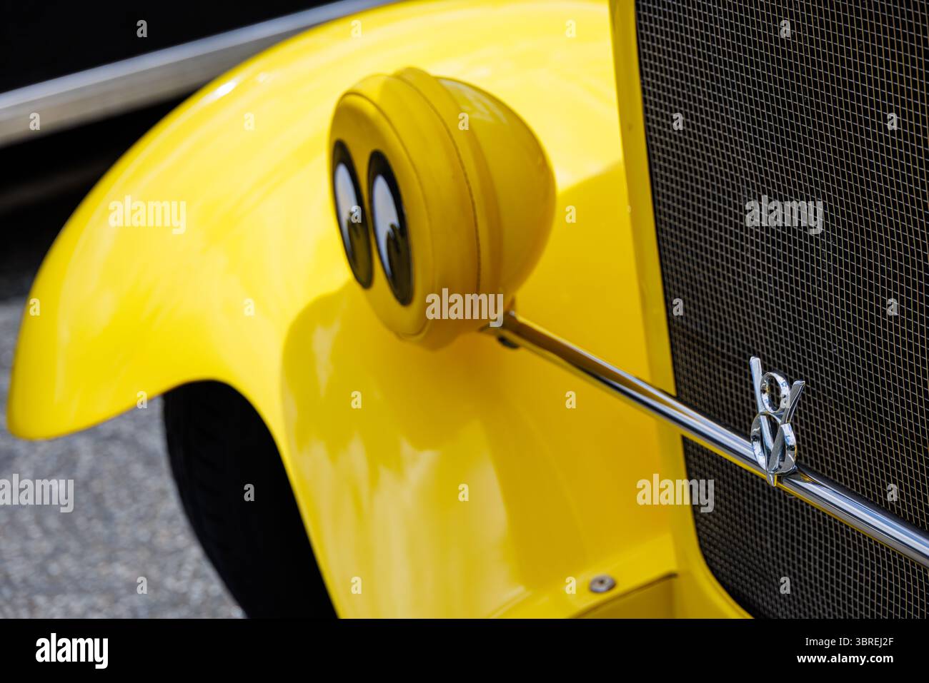 Gelbes Oldtimer mit Cartoonaugen auf dem Scheinwerfer und verchromtem Kühlergrill, der Humor und Charakter auf einer Oldtimer-Show zeigt. Stockfoto