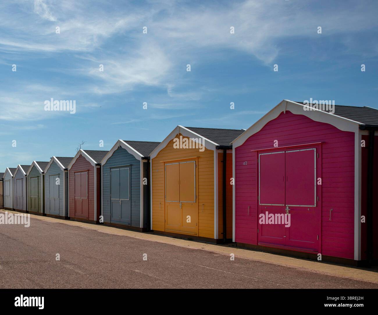 Eine Reihe von farbenfrohen Strandhütten erstreckt sich entlang der Promenade unter einigen schroffen strato-Zirruswolken am blauen Himmel. Stockfoto