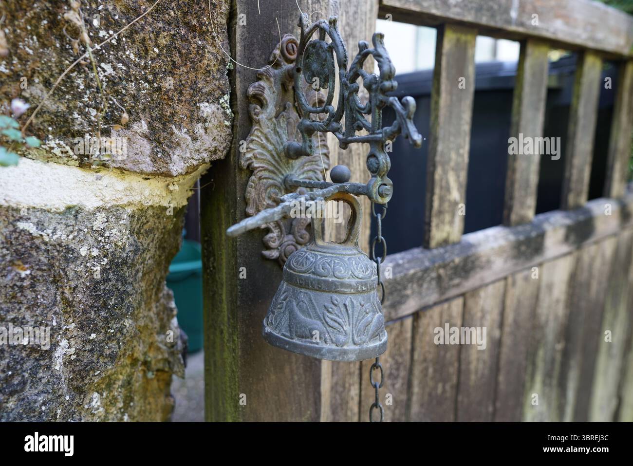 Rustikale Metallglocke an einem hölzernen Gartentor im Freien. Dorking, England Stockfoto