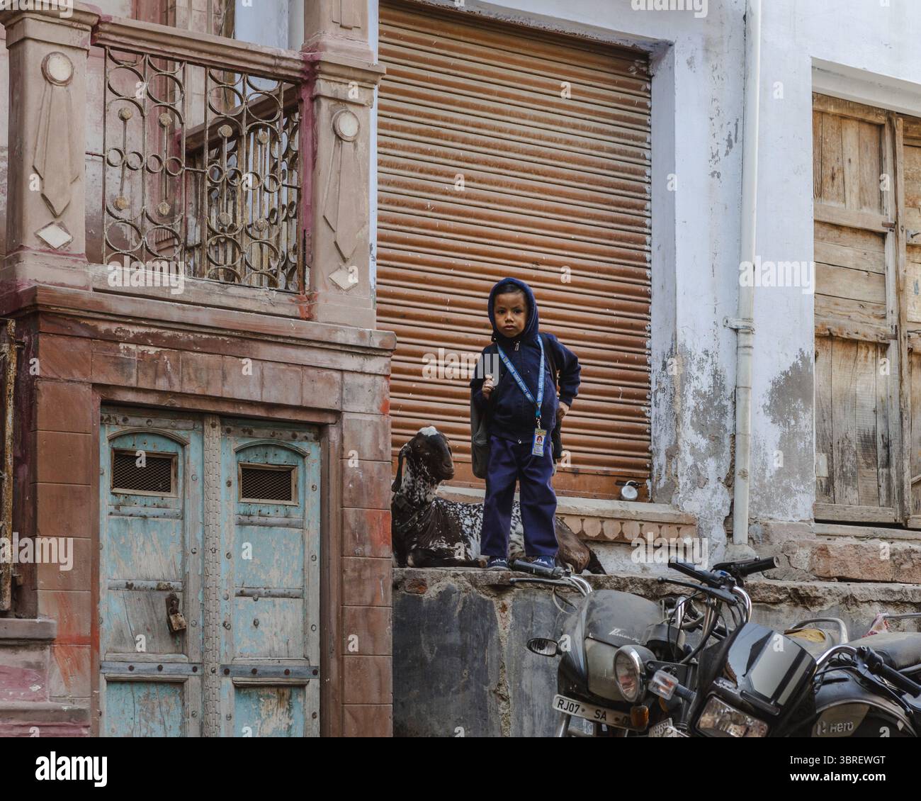 Bikaner, Indien - 24. Juni 2025: Blick auf ein Kind inmitten der rustikalen Architektur, verwitterten Fensterläden und dem leisen Motorrad, ein Tableau des ruhigen städtischen Lebens. Stockfoto
