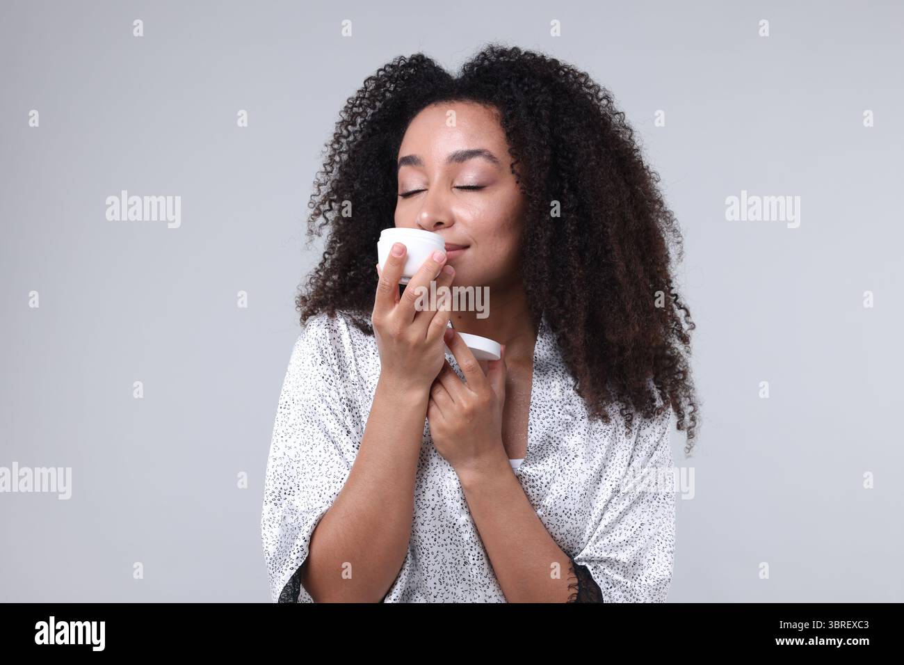 Schöne brasilianische Frau mit einem Glas Kollagencreme auf grauem Hintergrund Stockfoto