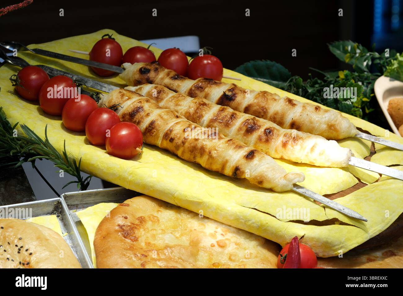 Drei Grillspieße liegen neben frischen Kirschtomaten auf einer hellen Servierplatte. Stockfoto