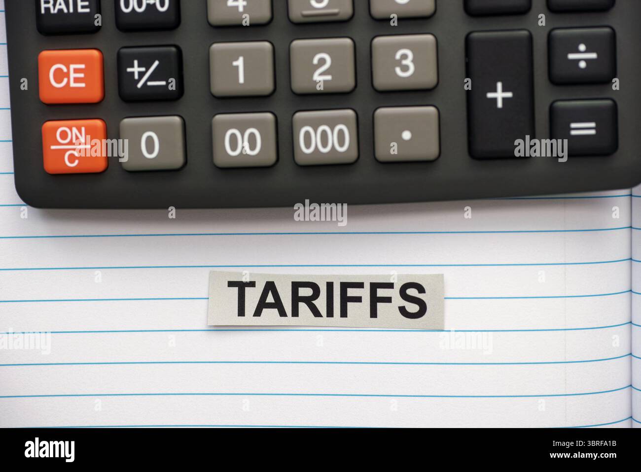 Ein grauer Streifen Papier mit dem Wort Tariffs, das in einem offenen Notizbuch in der Nähe eines Taschenrechners liegt. Stockfoto