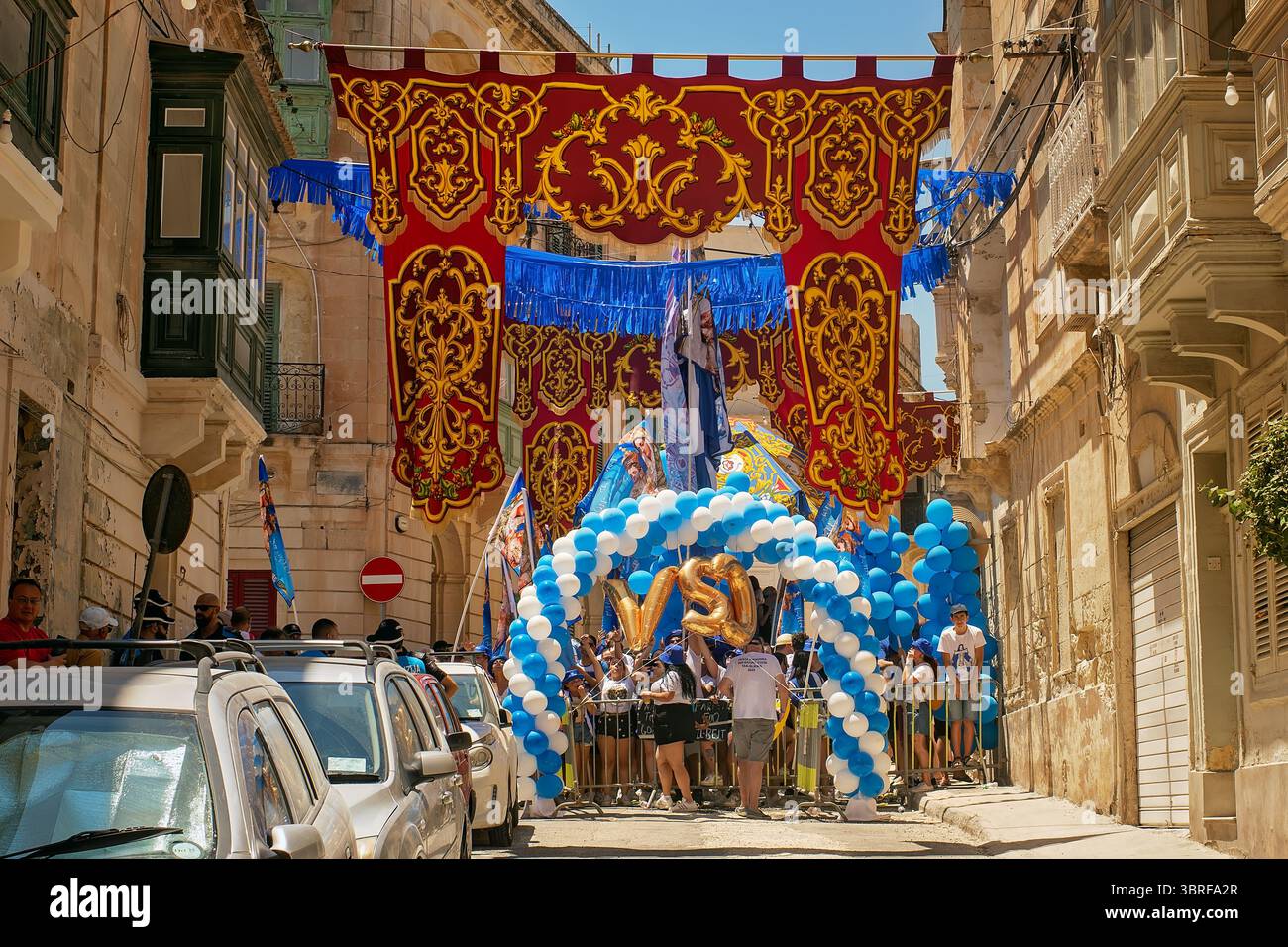 Sliema, Malta -07.06.2025: Eine belebte maltesische Straße in Sliema während einer religiösen Festa, dekoriert mit verzierten Bannern und blau-weißen Ballons Stockfoto