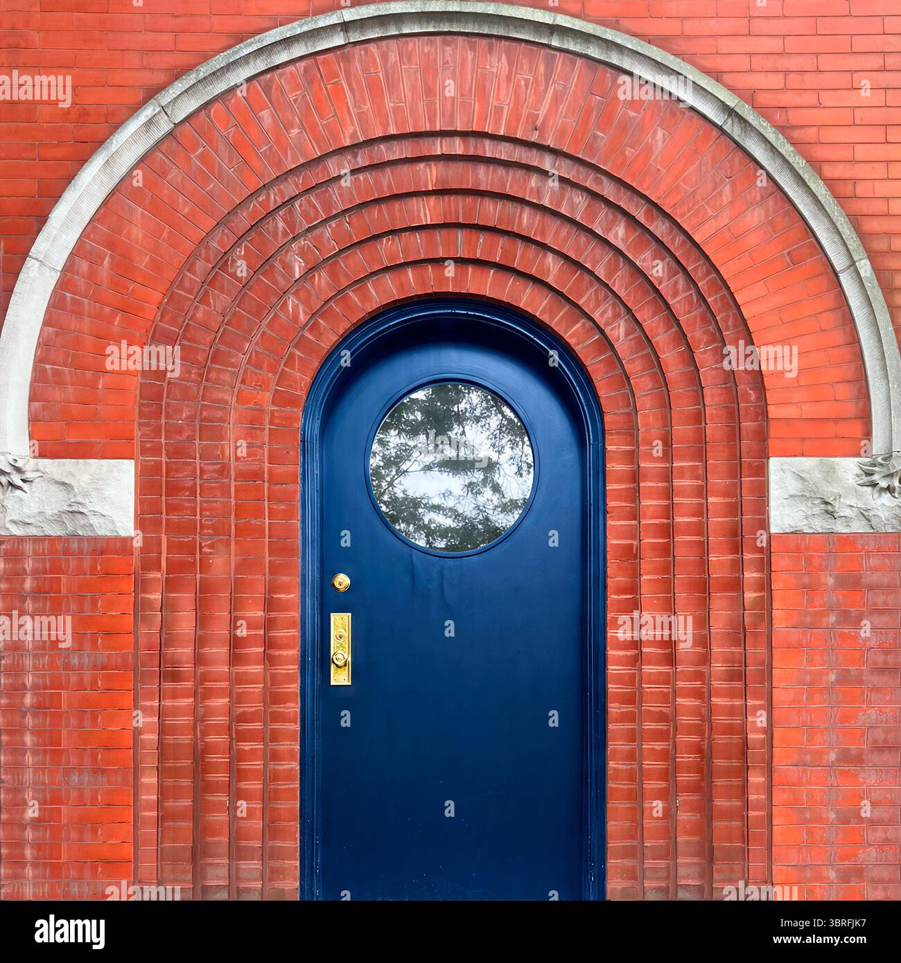 Die markante blaue Tür mit einem runden Fenster in konzentrischen roten Backsteinbögen und Steinakzenten – ein markantes architektonisches Statement in Chicago. - Smartphone-aufgenommenes Stockfoto