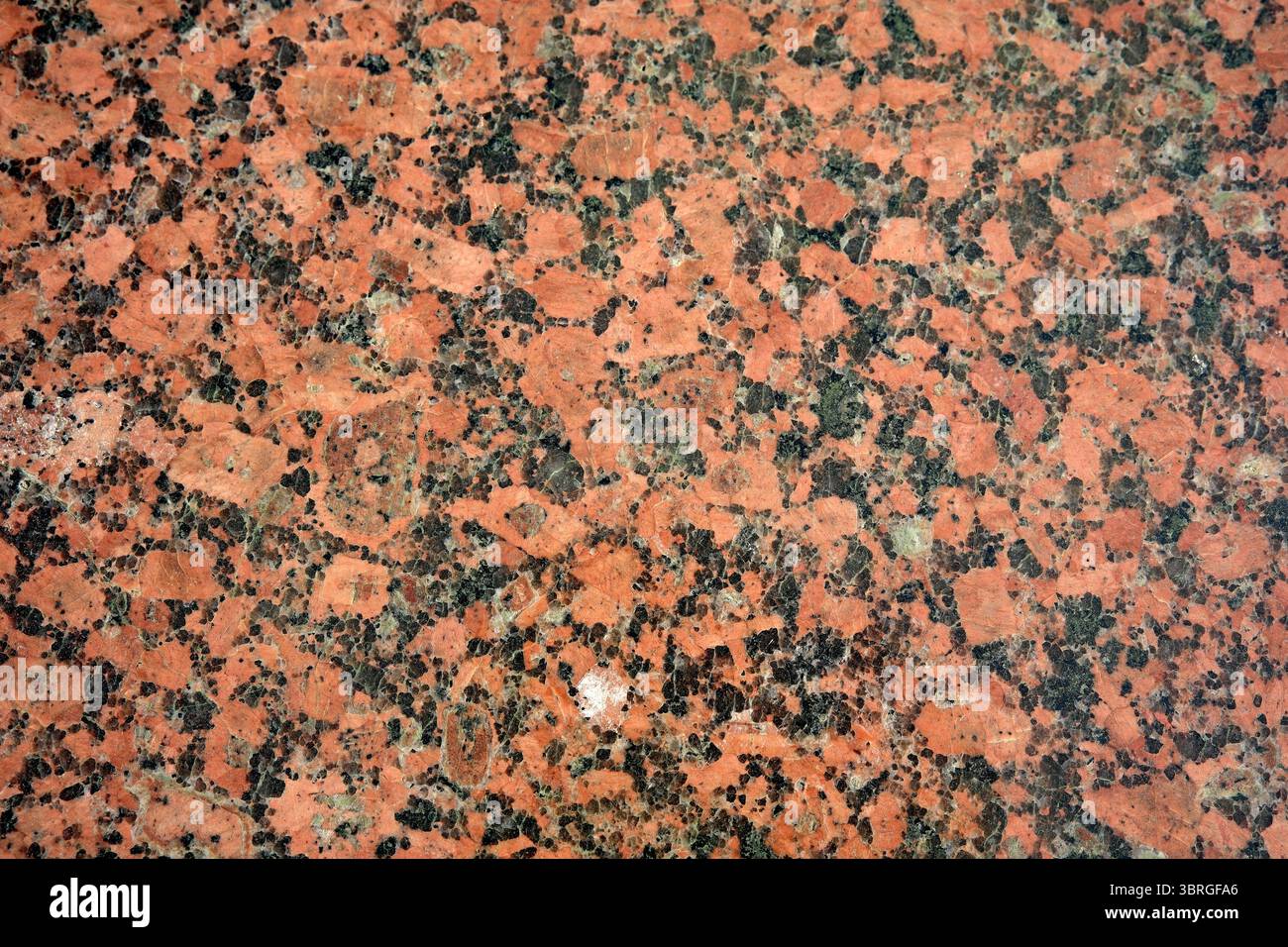 Nahaufnahme aus poliertem rotem Granit, das seine einzigartigen Texturen unterstreicht. Stockfoto