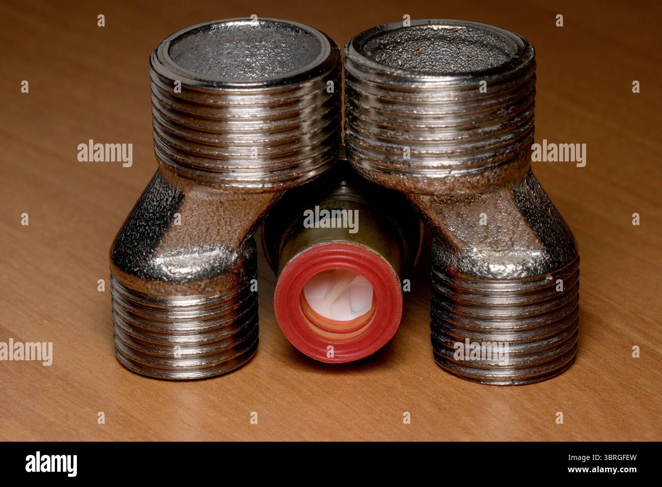 Drei metallische Rohrverschraubungen sorgen für ein markantes Erscheinungsbild auf poliertem Holz. Stockfoto