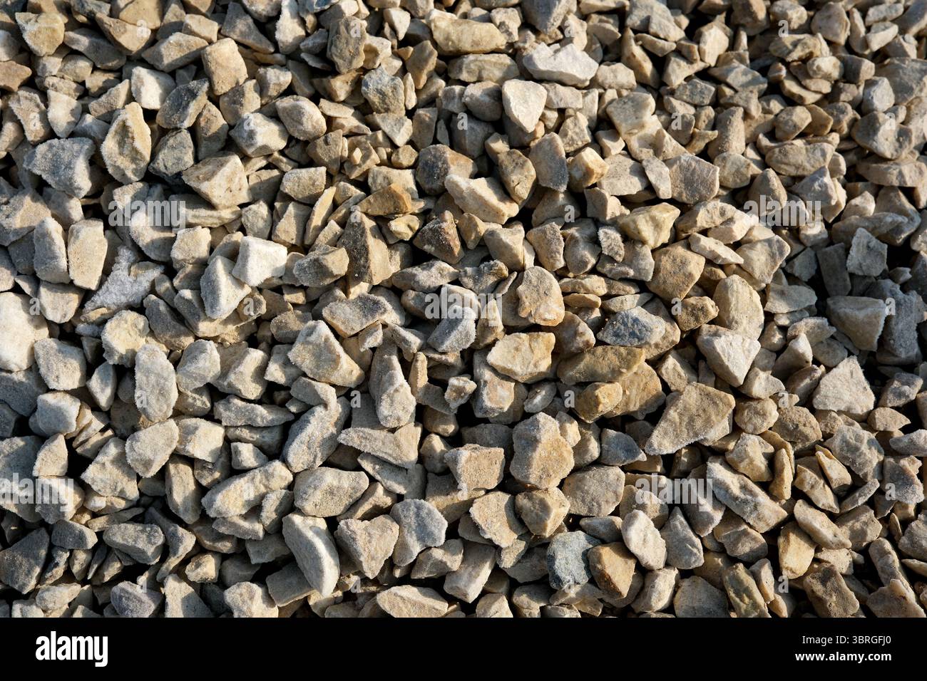 Kleine, raue Steine erzeugen eine natürliche Bodendecke, die im Sonnenlicht glitzert. Stockfoto