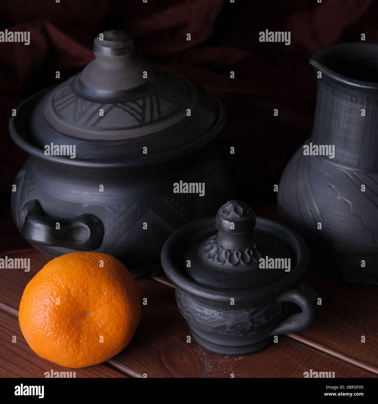 Handgefertigte schwarze Keramik ist wunderschön neben einem hellen Orange angeordnet. Stockfoto