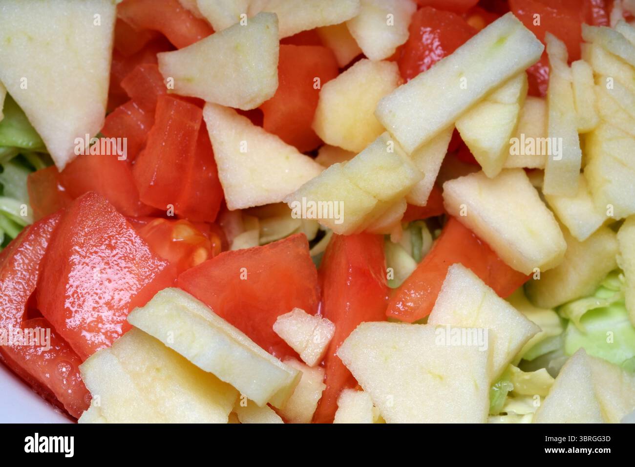 Eine bunte Mischung aus saftigen Tomaten und knusprigen Äpfeln wird sorgfältig auf einem Bett aus Blattgemüse angeordnet. Die einladende Atmosphäre der Küche ist ein Highlight Stockfoto