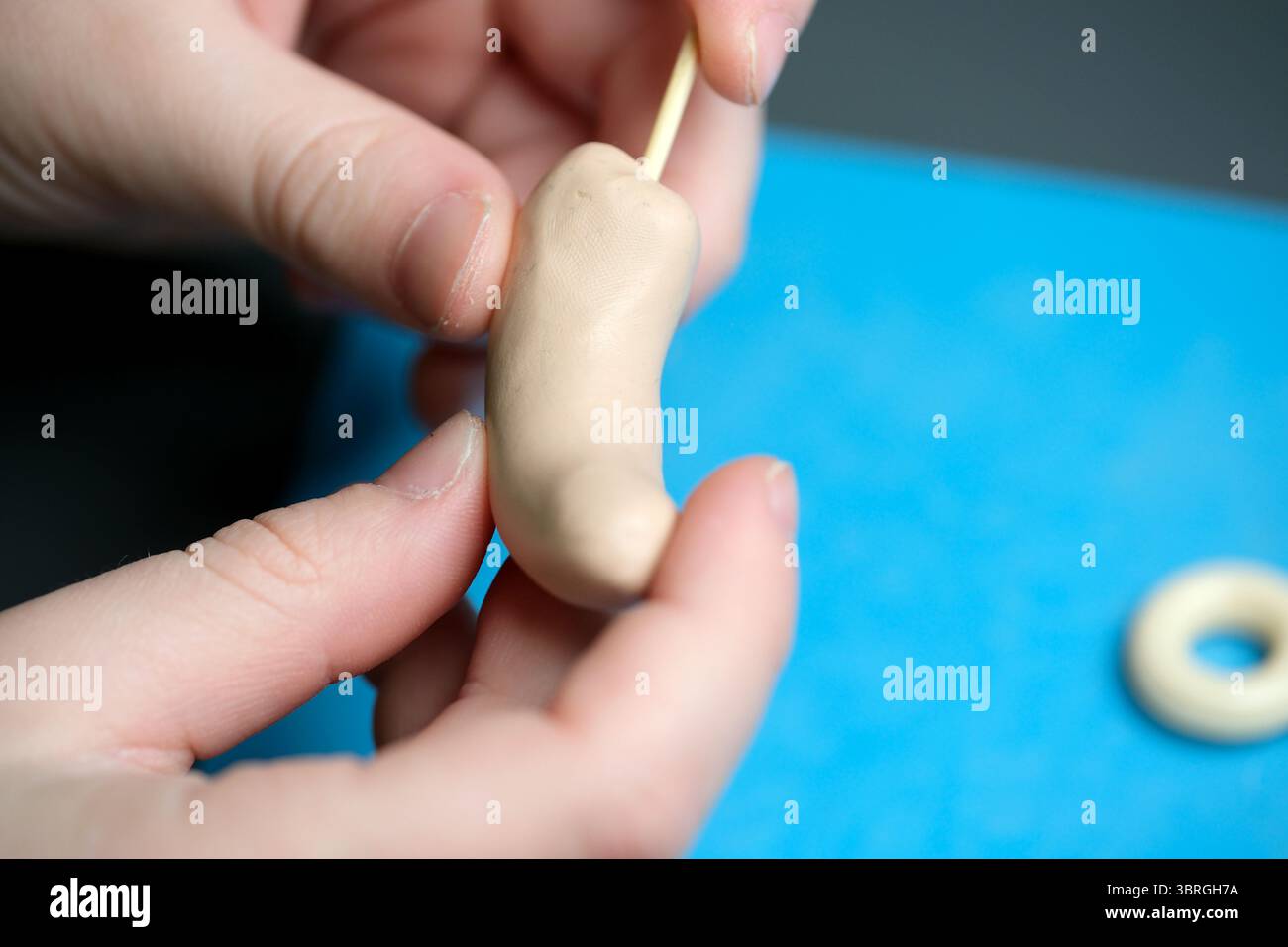 Die Hände Formen eine Figur aus weichem Ton, während ein Werkzeug den kreativen Prozess unterstützt. Stockfoto