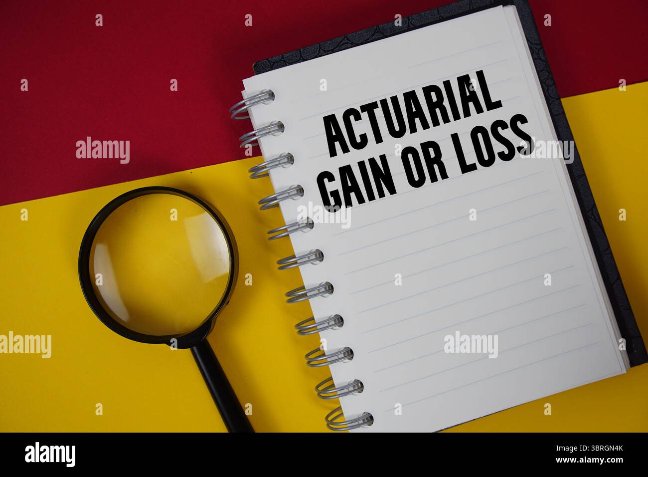 Text für versicherungsmathematische Gewinne oder Verluste, geschrieben auf Notizbuchpapier mit Lupe Stockfoto