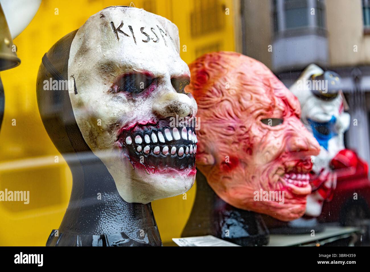 Gruselige Halloween-Masken zum Verkauf in einem Schaufenster, einschließlich einer gruseligen weißen Maske mit Kiss Me auf der Stirn. Groteske Horrormasken. Stockfoto