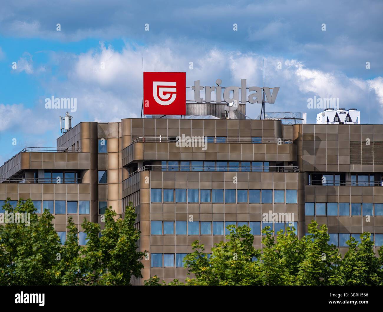 Ljubljana, Slowenien - 9. Juli 2025: Ein modernes Bürogebäude mit einem markanten roten Logo auf dem Dach. Die Fassade besteht aus einer Mischung aus Glas und Metall Stockfoto