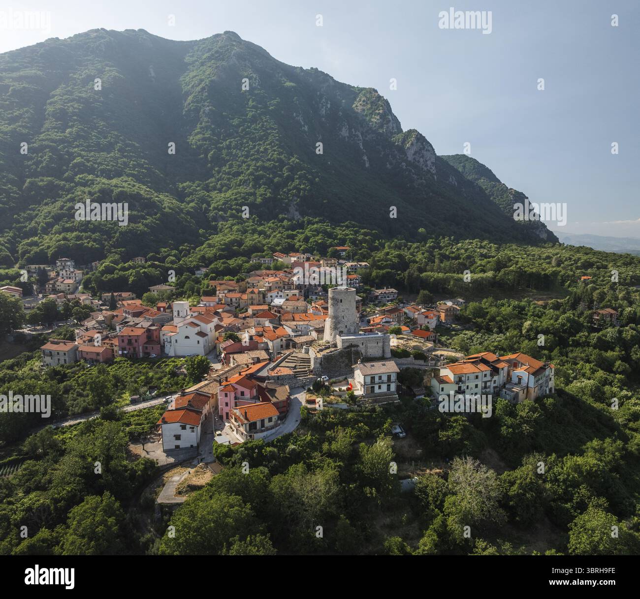 Blick aus der Vogelperspektive auf die Dächer von Terrakotta, die sich um den alten Turm gruppieren, vor dem Hintergrund der majestätischen grünen Berge, Summonte, Avellino, Italien. Stockfoto