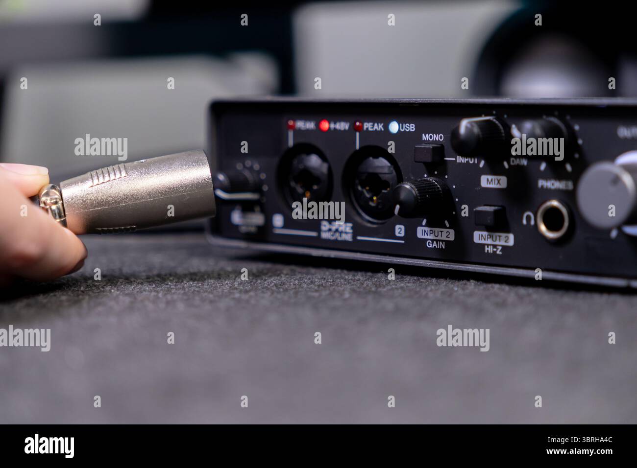 Nahaufnahme einer menschlichen Hand, die einen silbernen XLR-Audioanschluss in die Eingangsbuchse einer digitalen Soundkarte einsteckt, um die Einrichtung für die Studioarbeit anzuzeigen Stockfoto