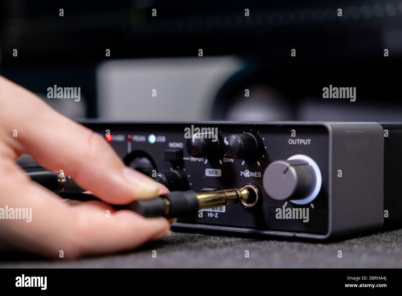 Nahaufnahme einer Hand, die ein Klinkenkabel mit Goldspitze in den Ausgang DES TELEFONS einer digitalen Audioschnittstelle einführt, die für Aufnahmen im Heimstudio und Musik entscheidend ist Stockfoto