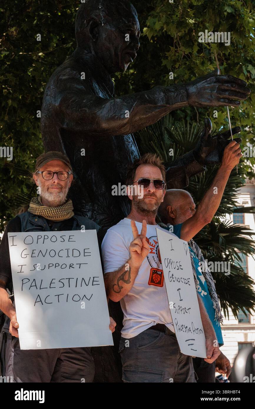 London, Großbritannien. Juli 2025. Demonstranten halten Schilder mit der Aufschrift "Ich bin gegen den Völkermord - ich unterstütze die Palästinensische Aktion" unter der Nelson Mandela Statue auf dem Parlamentsplatz. Es war der zweite solcher Protest auf dem Parlamentsplatz, der von der Wahlkampfgruppe verteidigt unsere Jurys organisiert wurde, seit das britische Parlament beschlossen hat, die direkte Aktionsgruppe Palestine Action ab dem 5. Juli 2025 als terroristische Organisation zu verbieten. Ähnliche Proteste fanden anderswo im Vereinigten Königreich statt. Alle Demonstranten mit Schildern wurden unter dem Terrorismusgesetz von 2000 wegen des Verdachts, eine verbotene Organisation zu unterstützen, verhaftet und könnten nun mit einer langen Pri konfrontiert sein Stockfoto