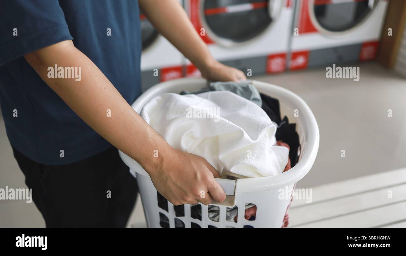 Hausmann mit Korb und schmutziger Wäsche gewaschene Kleidung im Waschraum. Waschmaschine im Wäschereigeschäft Konzept Stockfoto