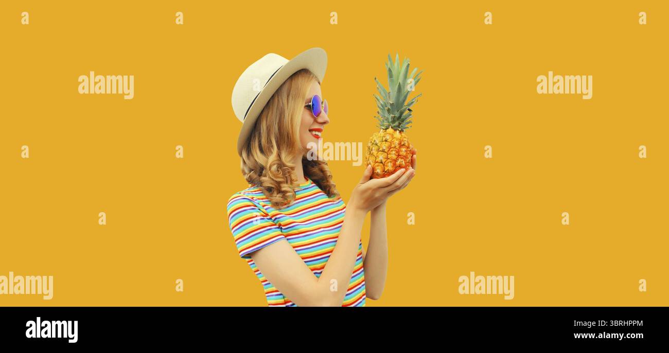 Sommerporträt einer glücklichen lächelnden jungen Frau mit Ananasfrucht im touristischen Strohhut, Sonnenbrille auf gelbem Studiohintergrund Stockfoto