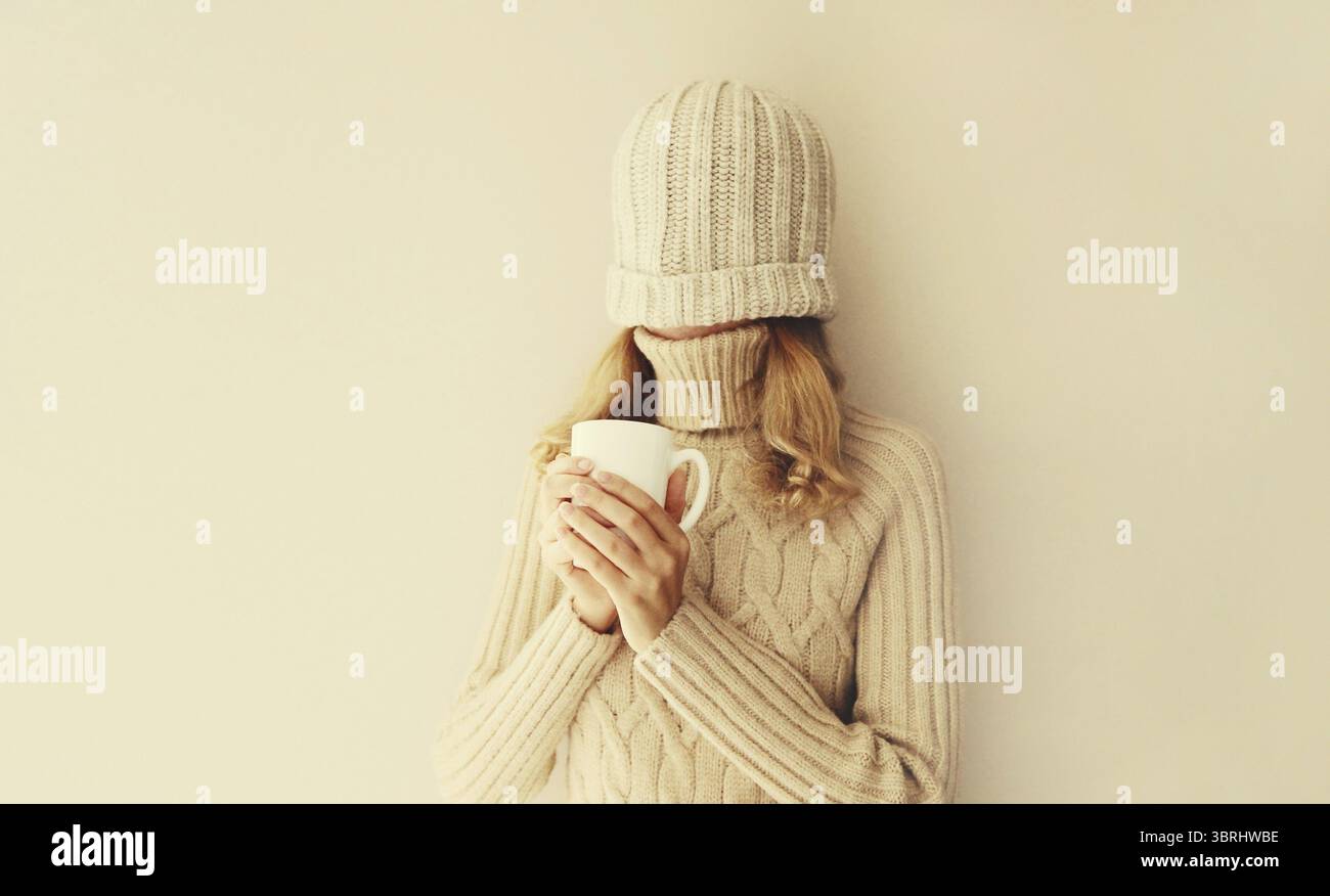 Glückliche lustige junge Frau mit einer Tasse Kaffee trinken im Winter gestrickte Hut, Pullover, der Spaß auf beigem Hintergrund hat Stockfoto