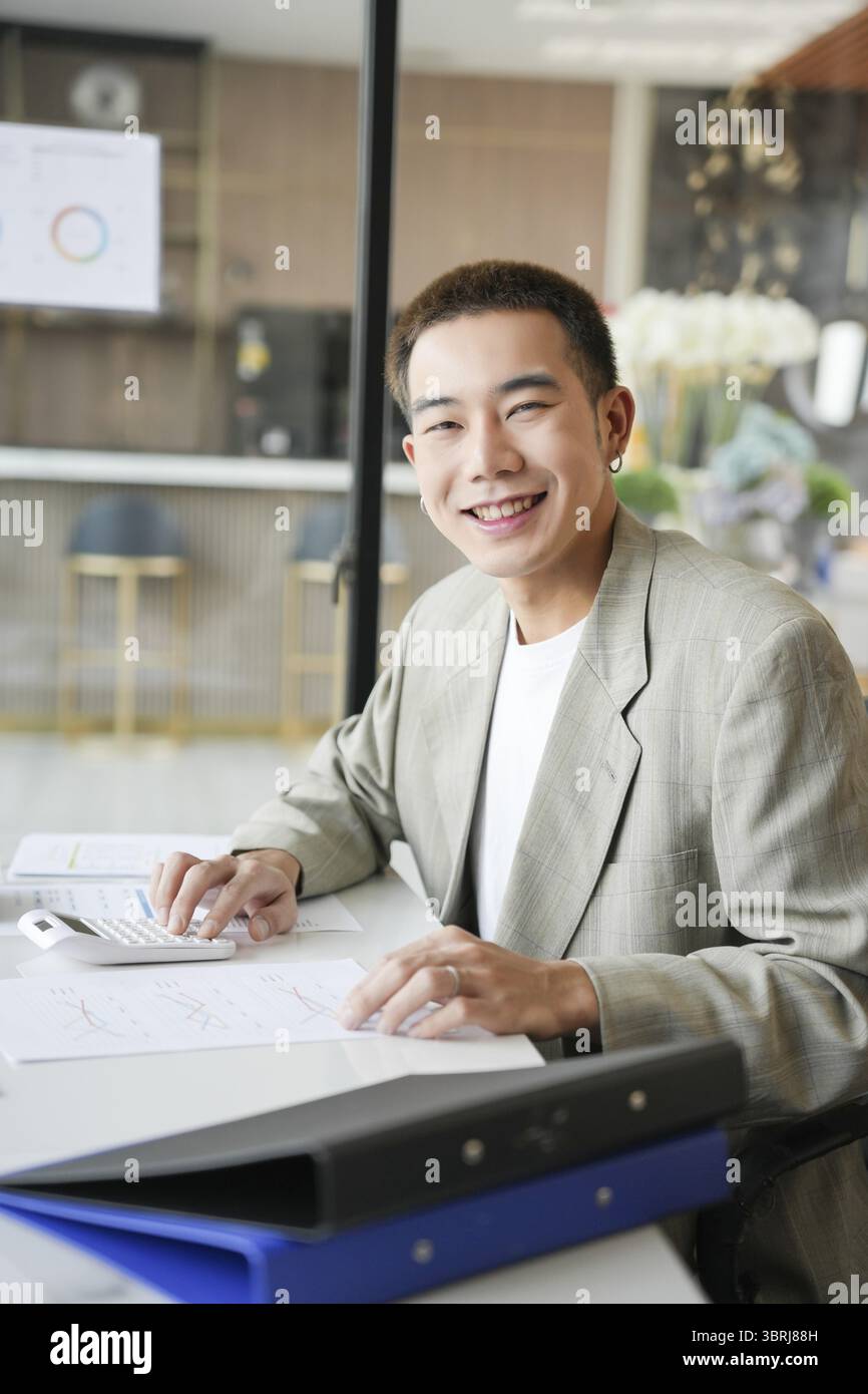 Lächelnder junger asiatischer Geschäftsmann im modernen Büro. Gutaussehender asiatischer Mann glücklich und freundlich während der Arbeit Erfolg Job Stockfoto
