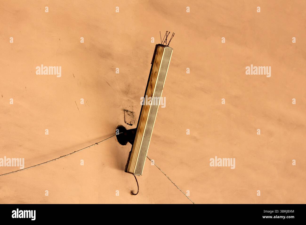 Ein hoher, rechteckiger Lautsprecher mit freiliegenden Drähten ist diagonal an einer pfirsichfarbenen Stuckwand montiert und veranschaulicht die Retro-Beschallungstechnik Stockfoto