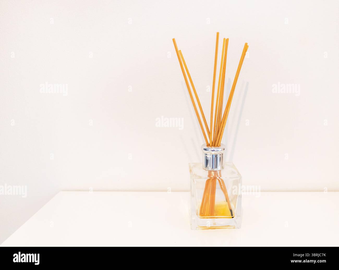 Minimalistischer Duftdiffusor mit orangefarbenen Stäbchen auf weißem Hintergrund. Stockfoto