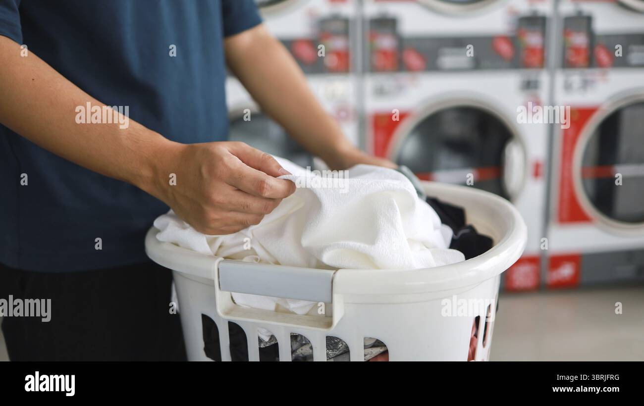 Hausmann mit Korb und schmutziger Wäsche gewaschene Kleidung im Waschraum. Waschmaschine im Wäschereigeschäft Konzept Stockfoto