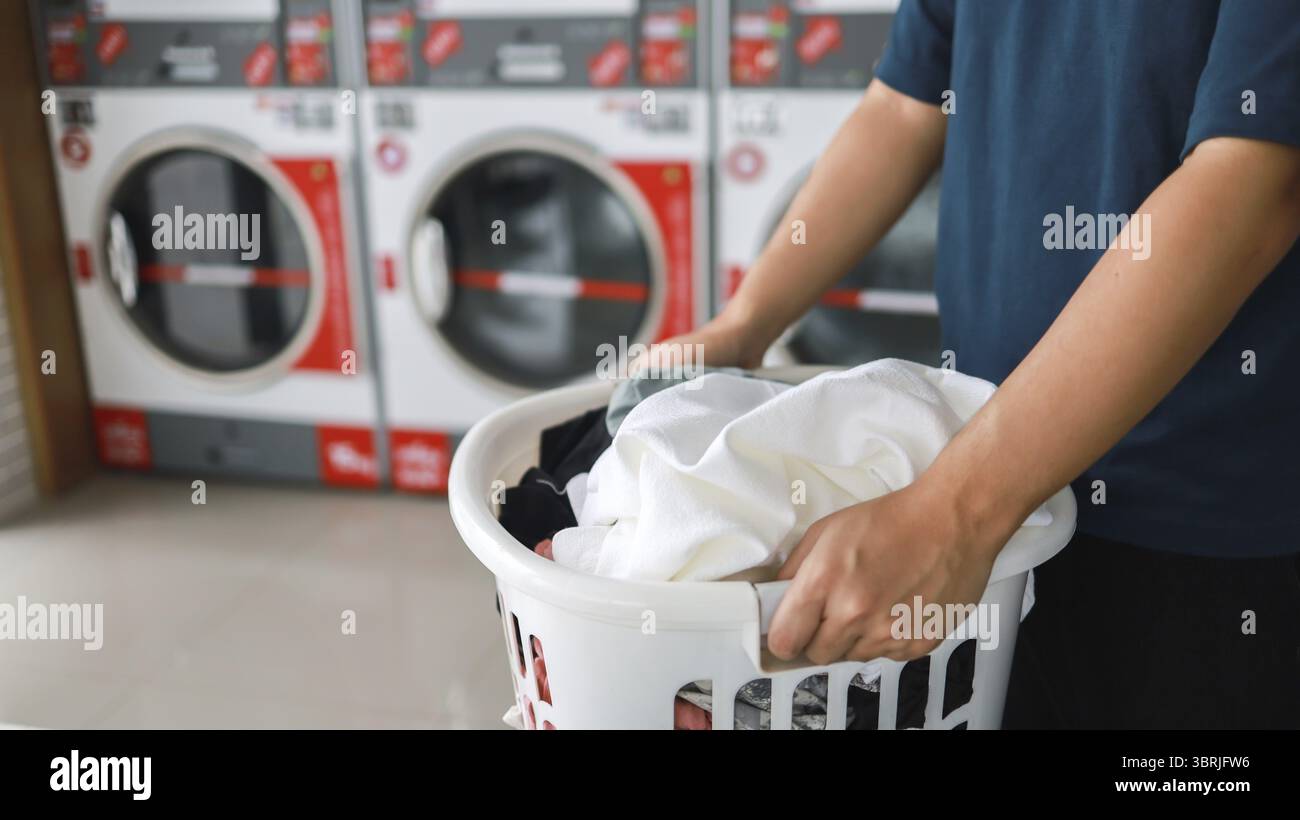 Hausmann mit Korb und schmutziger Wäsche gewaschene Kleidung im Waschraum. Waschmaschine im Wäschereigeschäft Konzept Stockfoto