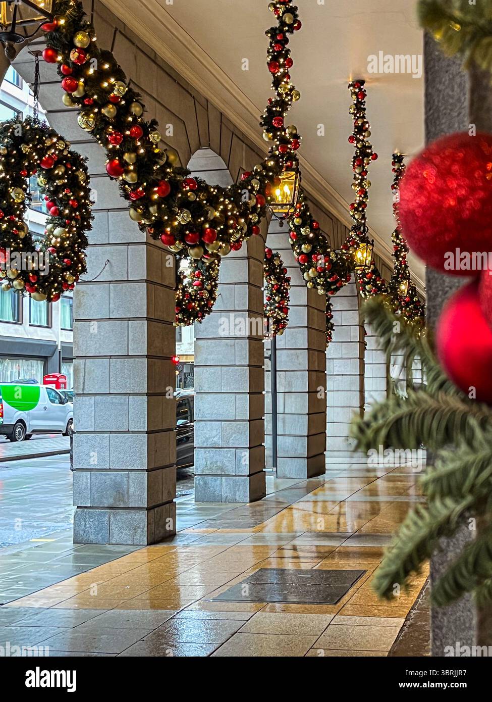 Weihnachtsdekorationen mit Girlanden und Ornamenten hängen an Steinsäulen und verstärken das festliche Ambiente der urbanen Umgebung im Winter ce Stockfoto